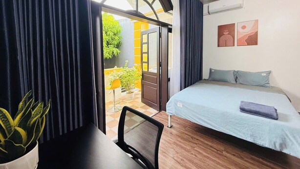 Una camera da letto con un letto, una scrivania e una sedia. Si vede una finestra con tende, una pianta in vaso e vista all'esterno.