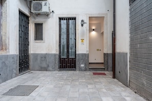 Une ruelle étroite avec un sol carrelé, un portail en métal, une petite fenêtre et une porte donnant sur un immeuble.