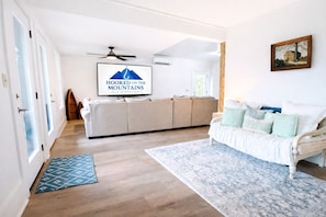Un vaste espace de vie comprenant un canapé, un tapis à motifs, un ventilateur de plafond et une œuvre d’art encadrée accrochée au mur.