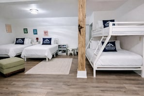 Une chambre d’hôtel avec deux lits simples, un lit superposé, un pouf vert, une petite table et un pilier blanc.