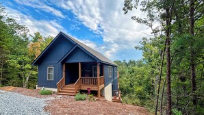 A blue cabin with a wooden porch, surrounded by a forest. - Wild Rose Cottage with Full Access to Rumbling Bald Amenities in Lake Lure! (Lake Lure)