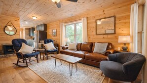 A cozy cabin interior with a wooden ceiling, a fireplace, a sofa, a rocking chair, and a dining table. - Wild Rose Cottage with Full Access to Rumbling Bald Amenities in Lake Lure! (Lake Lure)