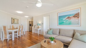Una sala de estar con sofá, una mesa de comedor con sillas, una zona de cocina y un cuadro grande con una playa.
