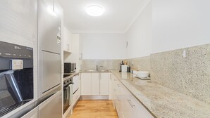 Una cocina moderna con muebles blancos, un refrigerador de acero inoxidable, un microondas y un fregadero.
