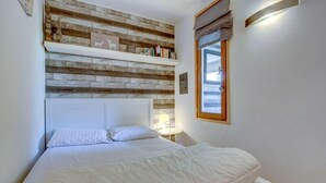 A bedroom with a wooden headboard, a bed with white bedding, a small table with a lamp, and a window with a curtain. - 3rd floor, balcony, parking, tv, ski locker, 35m², Morzine (Morzine)
