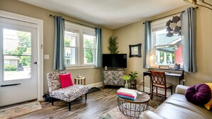 A living room with a sofa, a chair, a small table with books, a TV, and a decorative plant.