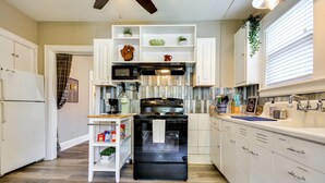 A kitchen with white cabinetry, a black oven, and a microwave. There are shelves with plants and kitchen items.