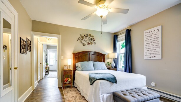 A bedroom with a bed, a ceiling fan, a bedside table with a lamp, a decorative wall piece, and a motivational quote on the wall.