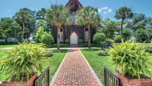 A church with a brick pathway leading to the entrance, surrounded by lush greenery and palm trees. - Lowcountry Landing! 3-story Townhouse in Old Town's Promenade (Bluffton)