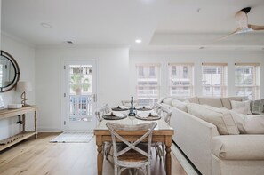 A spacious living area with a large sofa, a dining table with chairs, and a view of the outside through large windows.