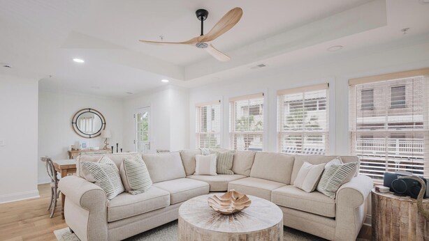 A spacious living room with a large L-shaped sectional sofa, a round wooden coffee table, and a ceiling fan. - Lowcountry Landing! 3-story Townhouse in Old Town's Promenade (Bluffton)