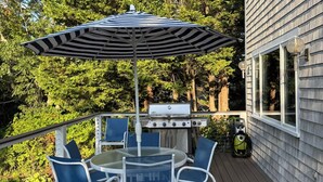A deck with a grill, blue chairs, and a striped umbrella.