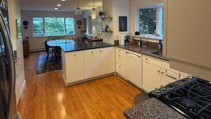 A modern kitchen with wooden flooring, white cabinets, granite countertops, and recessed ceiling lights.