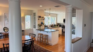 A modern kitchen with white cabinets, a central island, and a dining area with a wooden table and chairs.