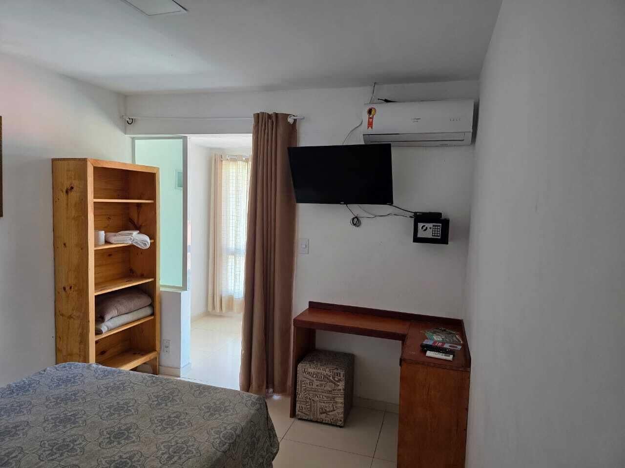 Une chambre comprenant un lit, une armoire en bois, un bureau avec une chaise, une télévision et un appareil de climatisation.