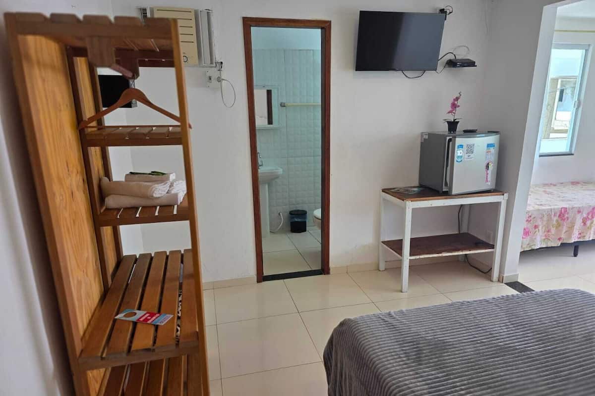 A hotel room with a wooden bench, a bed with a striped cover, a television on the wall, and a small table with a refrigerator.