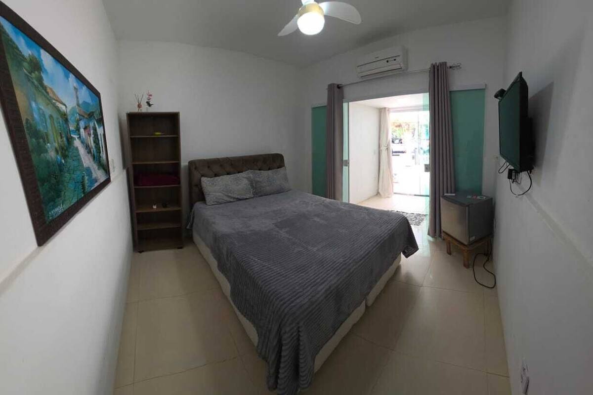 A bedroom with a bed, a ceiling fan, a TV, and a painting on the wall.