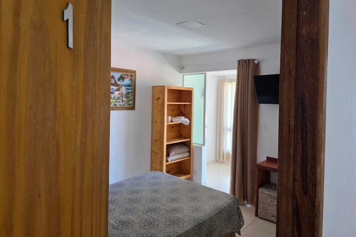 Una habitación con cama, un armario de madera, televisión y ventana con cortinas.