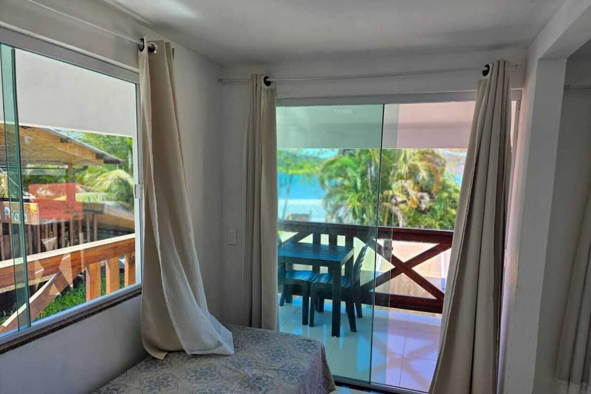 A room with a bed, a balcony with a table and chairs, and a view of the outdoors.