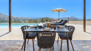 Un espacio de comedor al aire libre cubierto con una mesa preparada para dos, con vistas a una piscina y montañas.