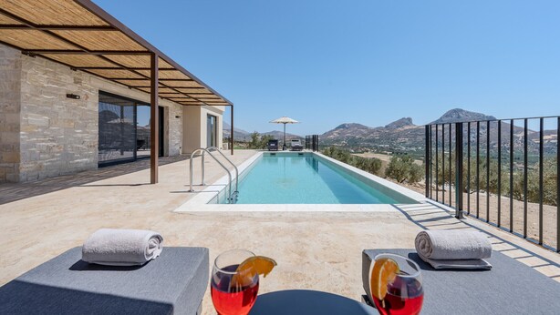 Un área de piscina con vista a las montañas, una zona de estar techada y un edificio de piedra.