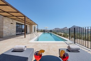 A pool area with a view of mountains, a covered seating area, and a stone building. - Filade Luxury Villa 1 (Agios Vasileios)