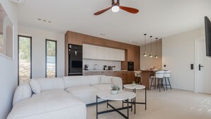 A modern kitchen with white cabinets, a dining area with a white sofa, and a ceiling fan. - Filade Luxury Villa 2 (Agios Vasileios)