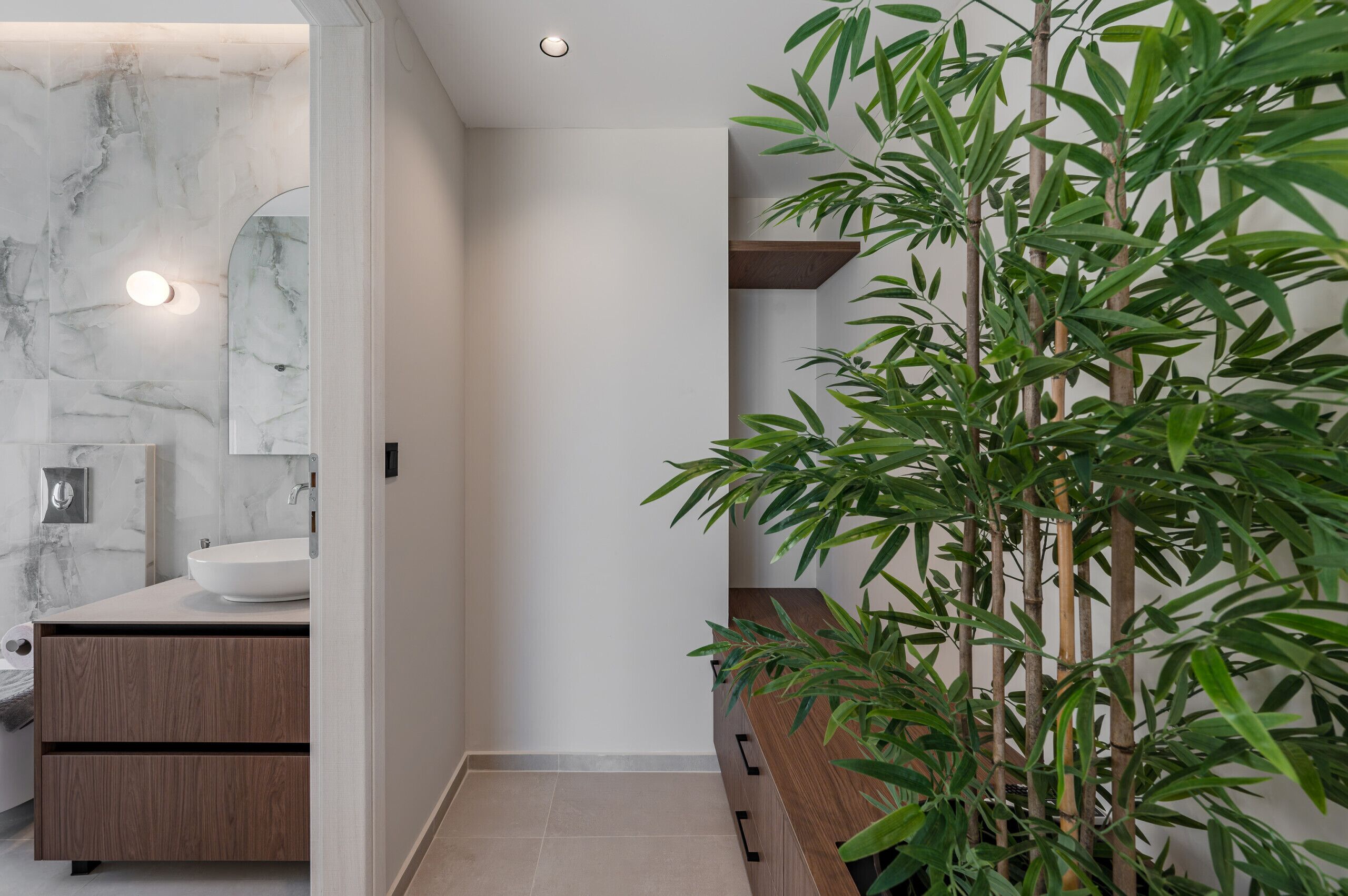 Een moderne badkamer met een marmeren wand, een houten wastafelmeubel en een bamboeplant.