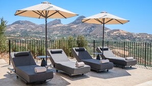 A terrace with four lounge chairs and two large umbrellas, overlooking a mountainous landscape. - Filade Luxury Villa 2 (Agios Vasileios)