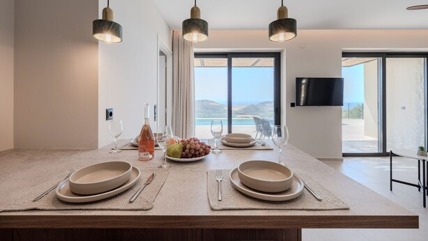 A modern kitchen with a central island, pendant lighting, and a view of the ocean. - Filade Luxury Villa 2 (Agios Vasileios)