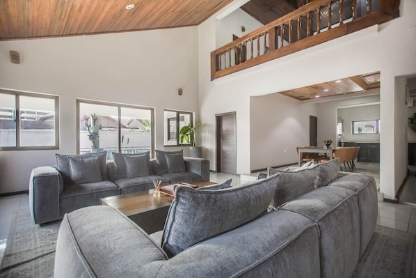A spacious living area with a large grey sectional sofa, a wooden coffee table, and a dining area with a table and chairs.