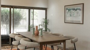 A modern dining area with a long table, six chairs, and a large window. - The Escape Ghana - Garden Villa (Accra)