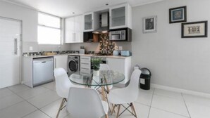 A modern kitchen with white cabinets, a glass dining table, and a black trash bin.