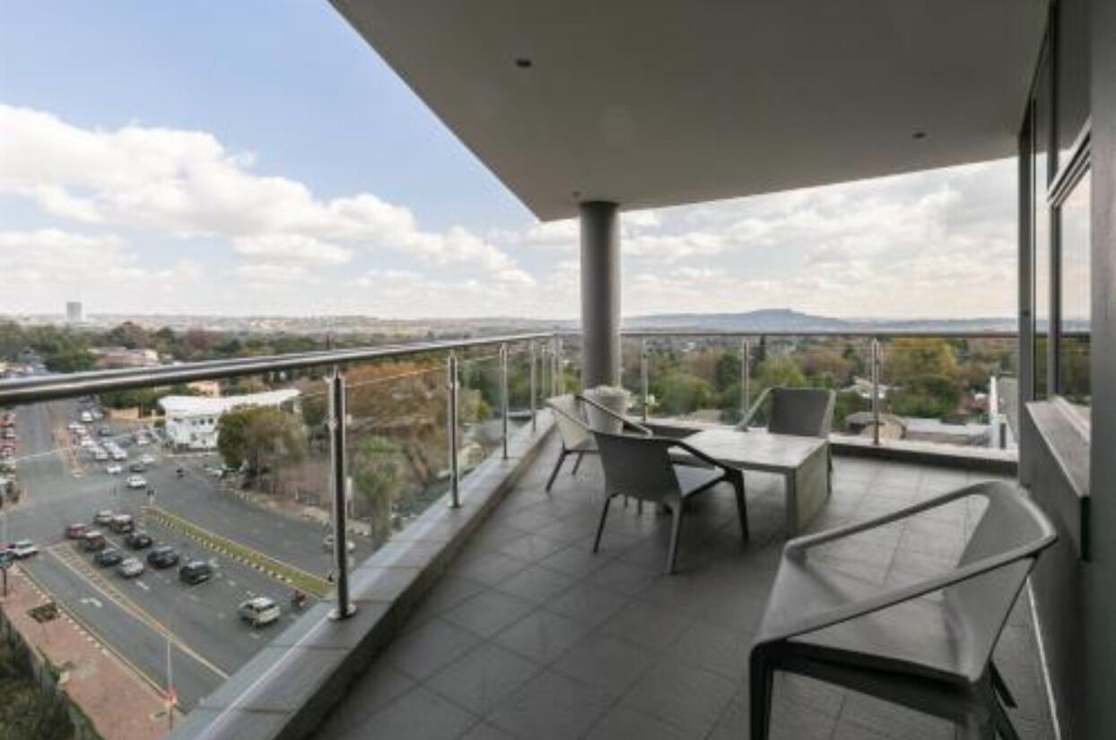 A balcony with a view of a cityscape, including a road and distant mountains.