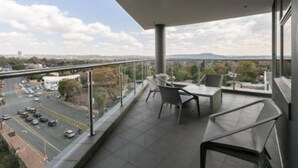 A balcony with a view of a cityscape, including a road and distant mountains.