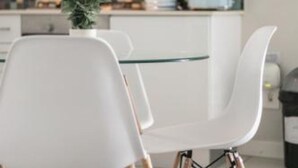 A modern kitchen with white cabinets, a glass table, and white chairs.