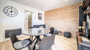 Ein modernes Wohnzimmer mit einem runden Glastisch, grau gepolsterten Stühlen, einer Holz-Akzentwand und einer Wanduhr.