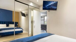 A modern hotel room with a large bed, a TV mounted on the wall, and a sliding door leading to a balcony.