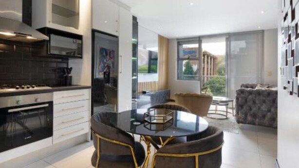 A modern kitchen with a dining area, featuring a round table and chairs, a built-in oven, and a large window offering a view.
