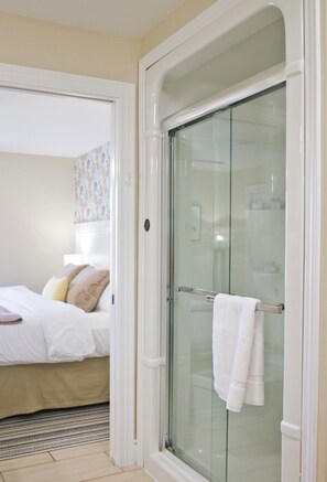 Quarto de hotel com cama, box de vidro para o chuveiro e área de banheiro visível.