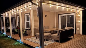 A covered outdoor area with a wooden deck, seating, and string lights.