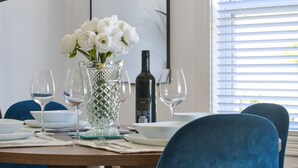 A dining table set with white flowers, wine glasses, and a bottle. Blue chairs surround the table.