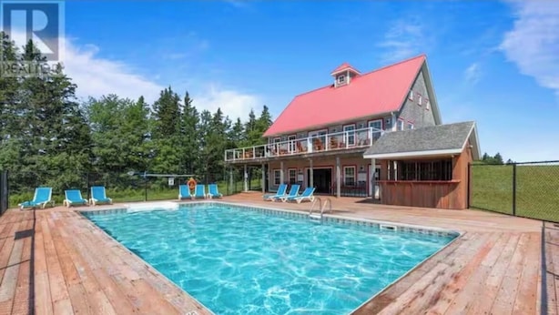 A wooden deck with a swimming pool, lounge chairs, and a building with a red roof.
