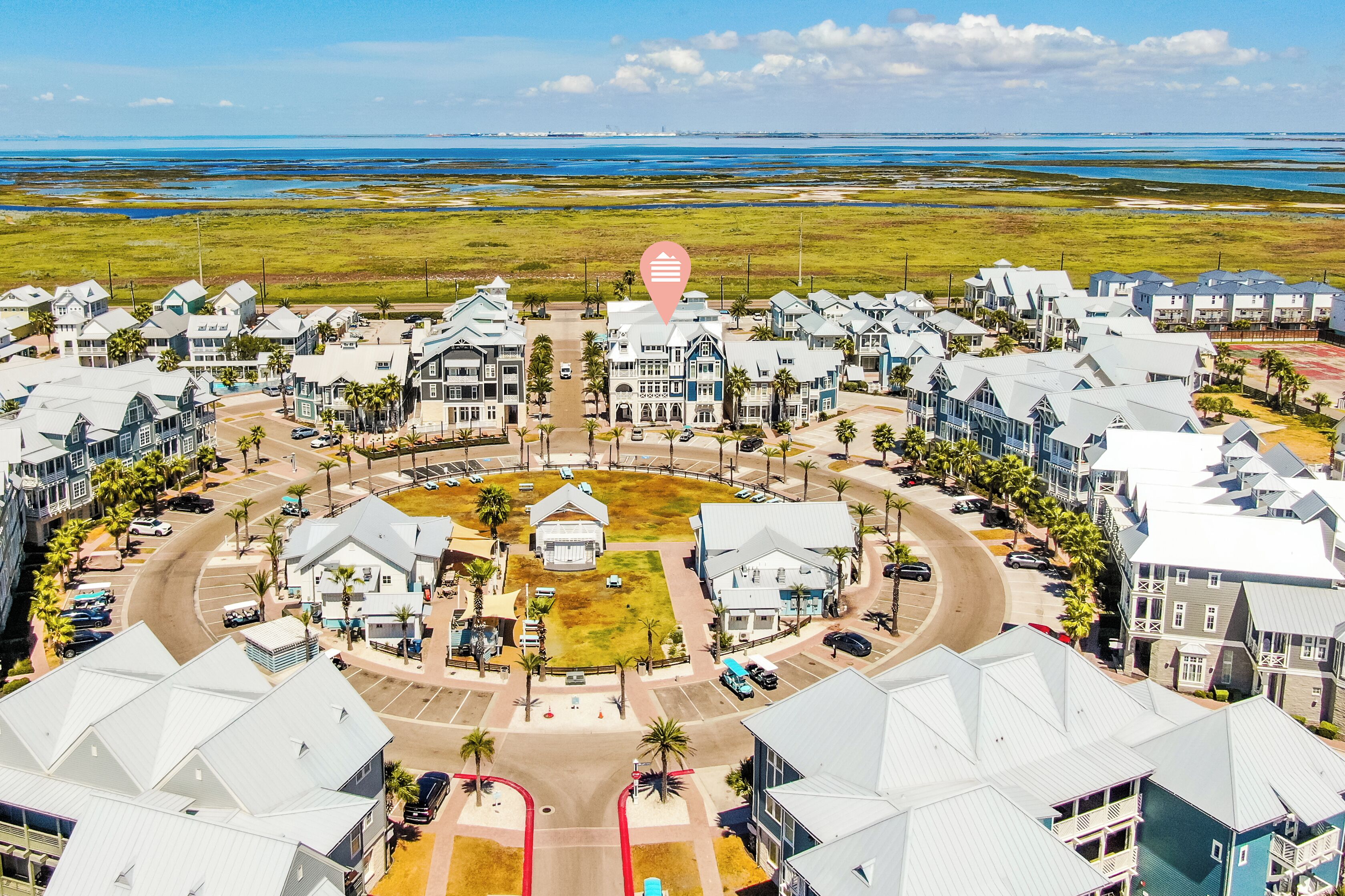 A coastal residential area with a central roundabout, surrounded by houses with gabled roofs, and a view of the ocean in the distance.