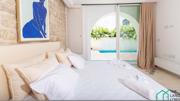 A hotel room with a large bed, a painting on the wall, and a view of a swimming pool through a glass door. - Le Duplex du Golden Tulip (La Marsa)