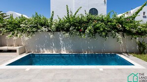 A swimming pool with a white wall and greenery overhead. - Le Duplex du Golden Tulip (La Marsa)