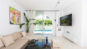 A modern living room with a sofa, coffee table, and TV. There's a large window with a view of greenery and a pool. - Le Duplex du Golden Tulip (La Marsa)