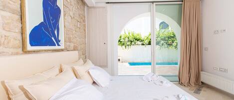 A hotel room with a large bed, a painting on the wall, and a view of a swimming pool through a glass door.