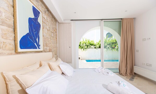 A hotel room with a large bed, a painting on the wall, and a view of a swimming pool through a glass door.