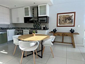 Uma cozinha moderna com armários brancos, uma mesa de jantar de madeira e um quadro pendurado na parede.